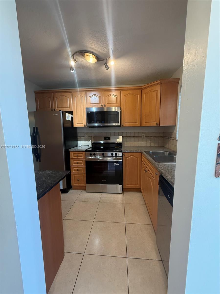 A kitchen features light wood cabinets, stainless steel appliances, and beige tile flooring — 5080 SW 64th Ave # 104, Davie FL 33314, DAVIE, FL