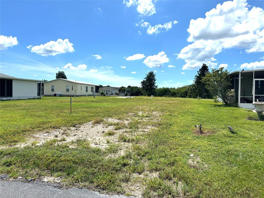 A vacant grassy lot sits between two manufactured homes under a bright blue sky — 659 LA SALA, NORTH PORT, FL