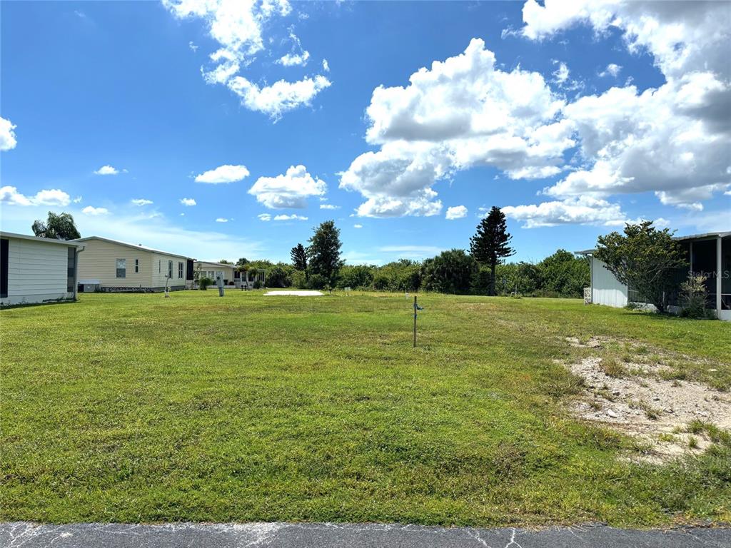 A vacant grassy lot sits between two mobile homes under a bright, cloudy sky — 659 LA SALA, NORTH PORT, FL