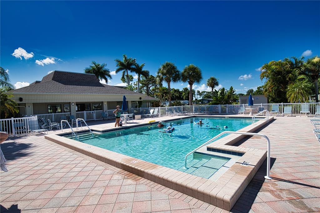 A rectangular swimming pool with a tiled deck is surrounded by palm trees and buildings — 659 LA SALA, NORTH PORT, FL