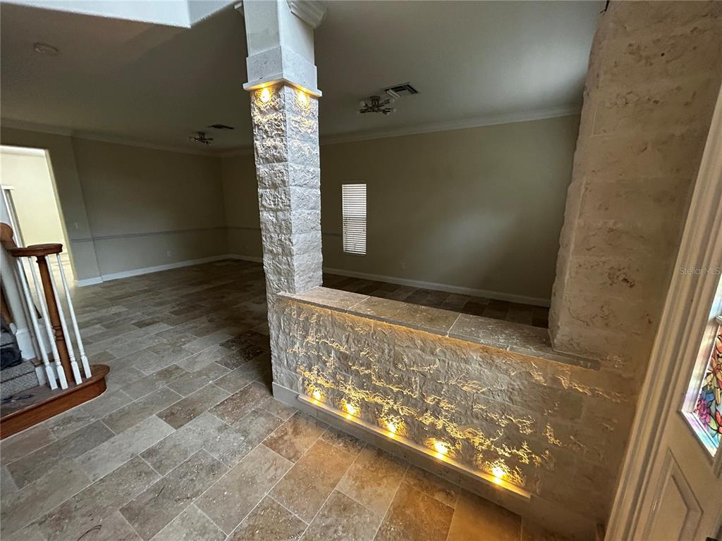 A stone-clad half wall with integrated lighting separates a tiled entryway from a living area — 6850 DOLCE STREET, ORLANDO, FL