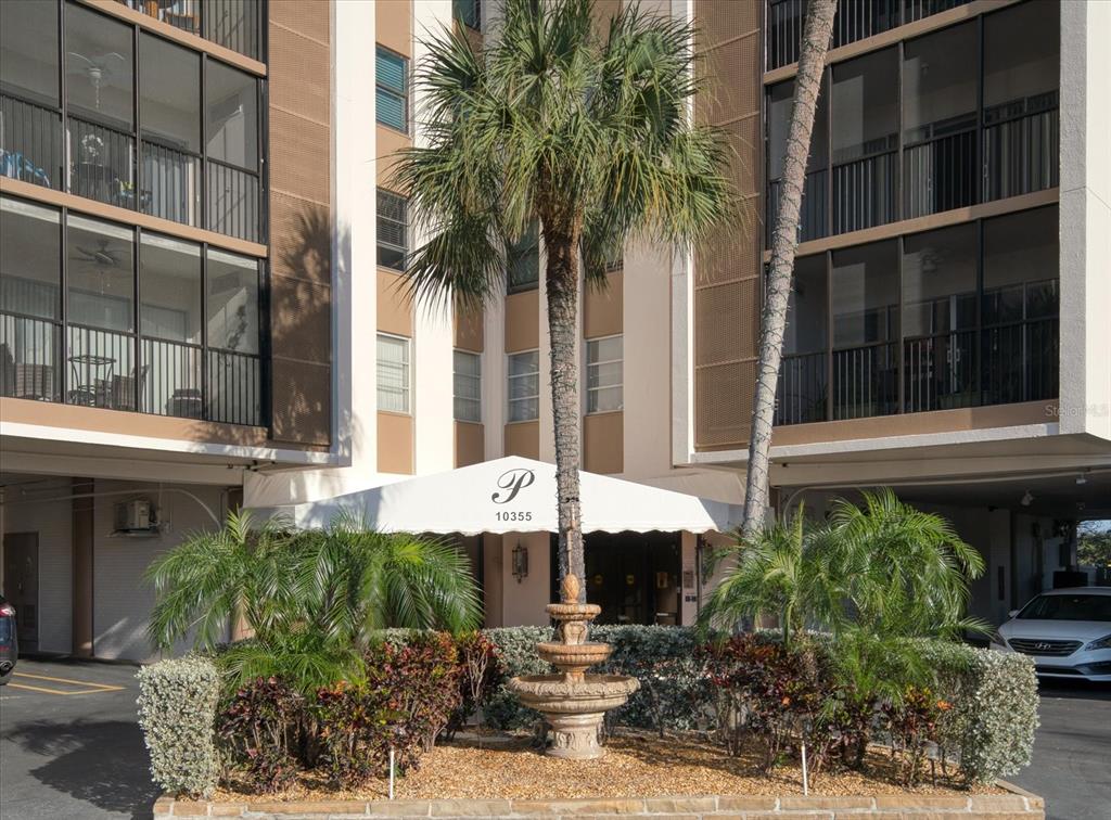 An exterior view of a building entrance featuring a fountain, palm trees, and a canopy — 10355 PARADISE BOULEVARD UNIT 612, TREASURE ISLAND, FL