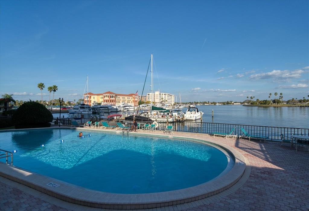 A swimming pool overlooks a marina with boats and buildings under a clear blue sky — 10355 PARADISE BOULEVARD UNIT 612, TREASURE ISLAND, FL
