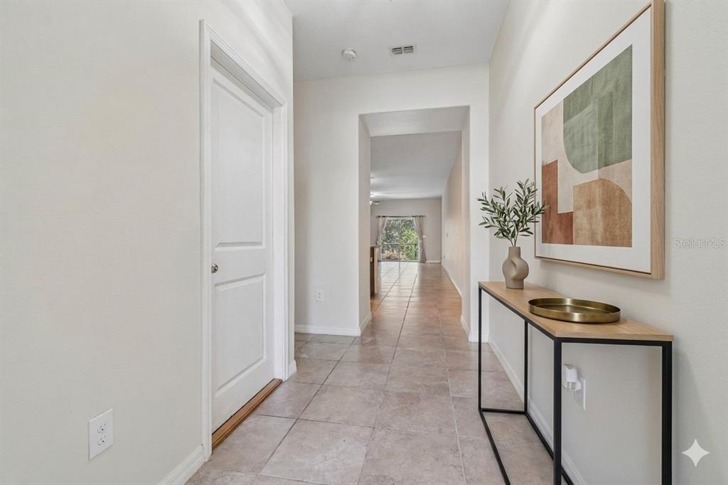 A tiled hallway features a white door, a console table, and a view toward windows — 10687 LAKE MONTAUK DRIVE, RIVERVIEW, FL