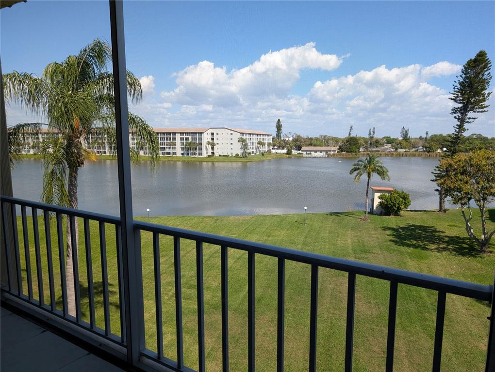 A balcony view overlooking a grassy lawn, a lake, and a multi-story apartment building — 3807 LAKE BAYSHORE DRIVE UNIT H-416, BRADENTON, FL