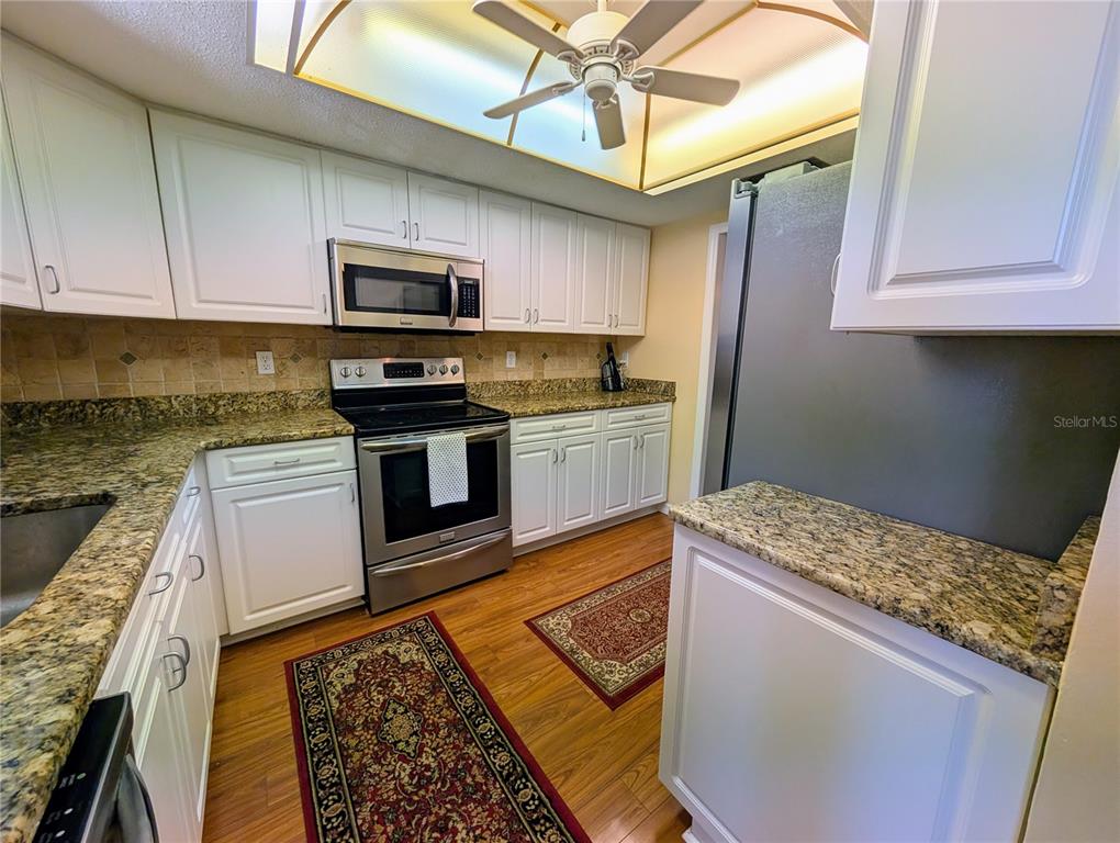 A kitchen features white cabinets, granite countertops, stainless steel appliances, and wood-look flooring — 3807 LAKE BAYSHORE DRIVE UNIT H-416, BRADENTON, FL