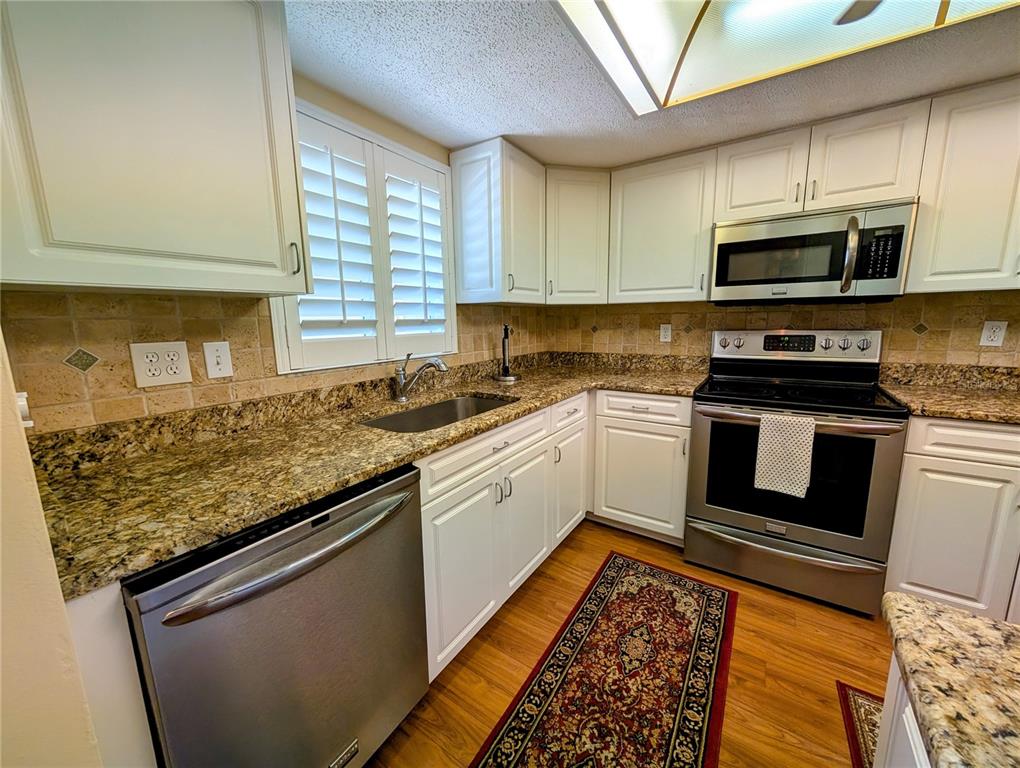 A kitchen with white cabinets, granite countertops, stainless steel appliances, and wood-look flooring — 3807 LAKE BAYSHORE DRIVE UNIT H-416, BRADENTON, FL