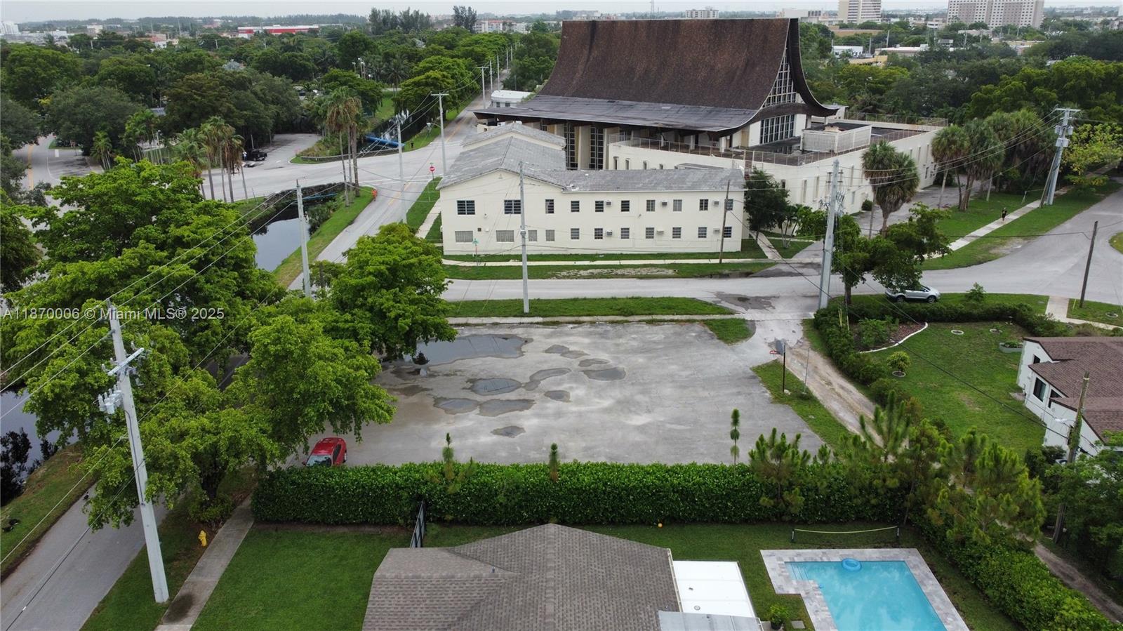 An aerial view shows a vacant paved lot adjacent to a large church and residential buildings — 425 Esplanade Dr, Miami Springs FL 33166, MIAMI SPRINGS, FL
