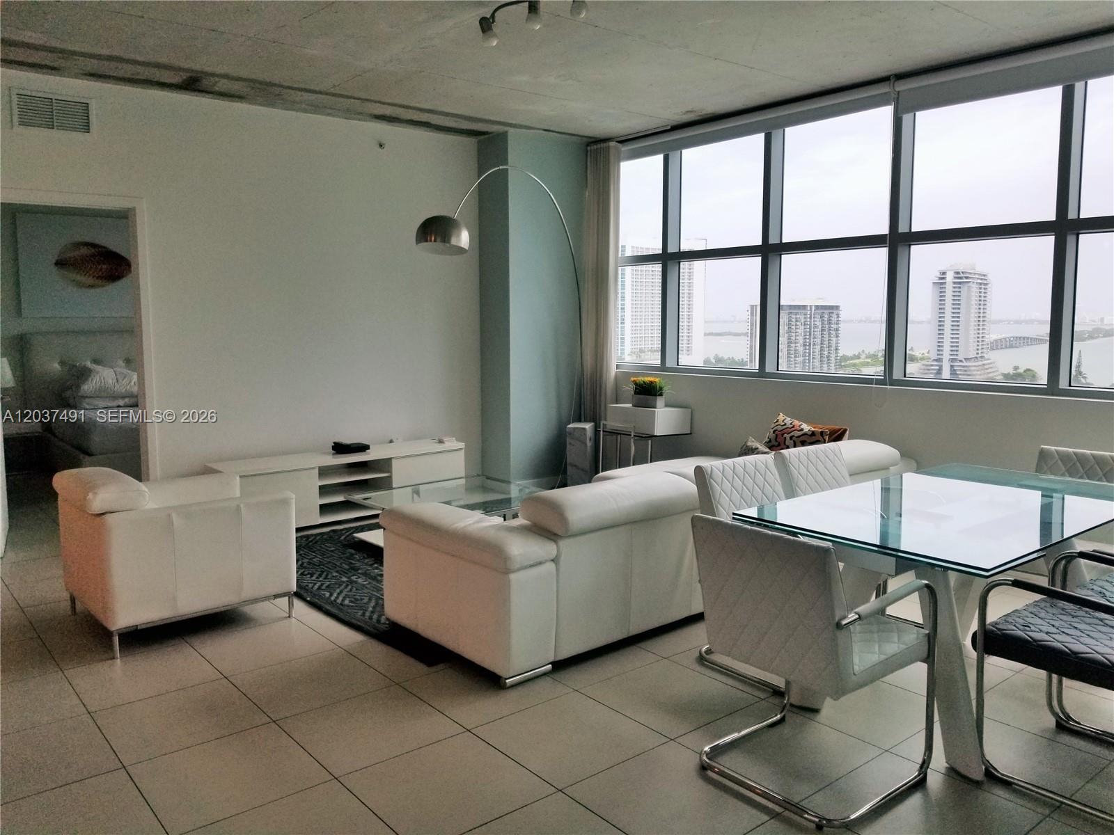 A modern living and dining area features white leather furniture, tile flooring, and floor-to-ceiling windows — 3301 NE 1st Ave # 1602, Miami FL 33137, MIAMI, FL