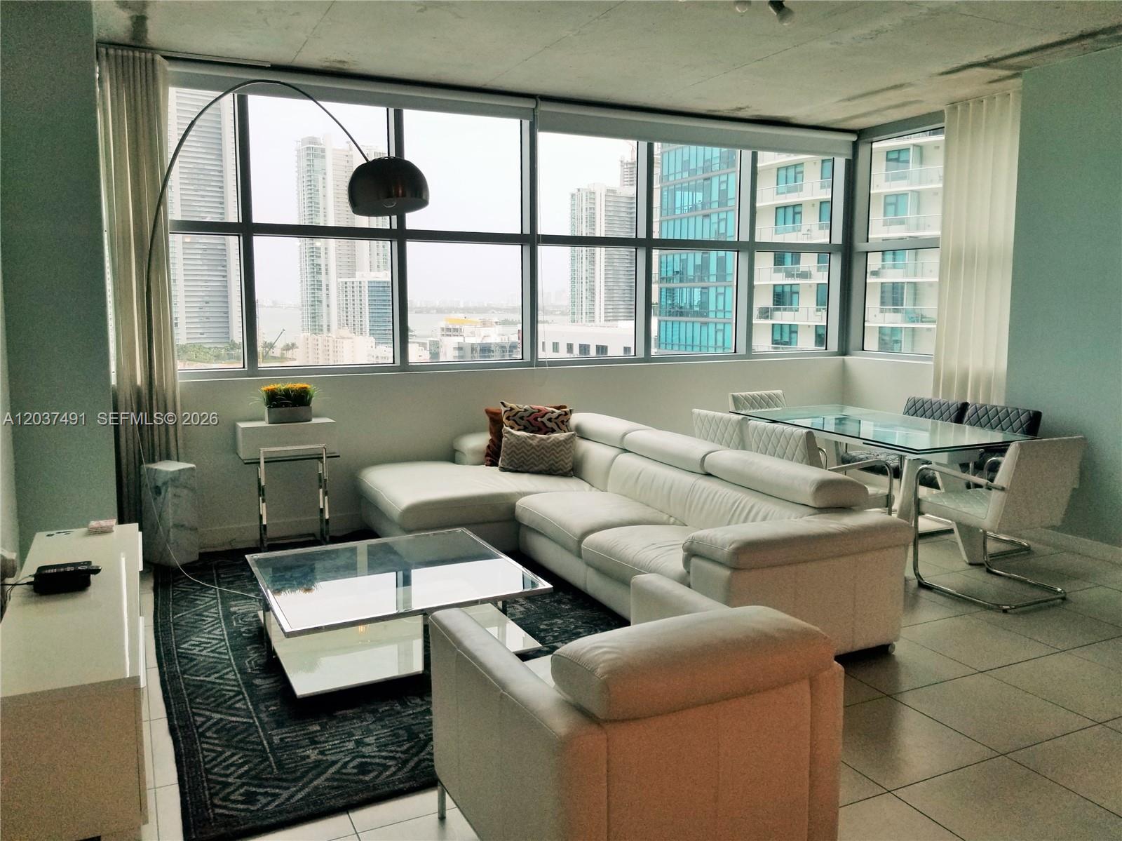 A modern living room features a white sectional sofa, glass coffee table, and floor-to-ceiling windows — 3301 NE 1st Ave # 1602, Miami FL 33137, MIAMI, FL