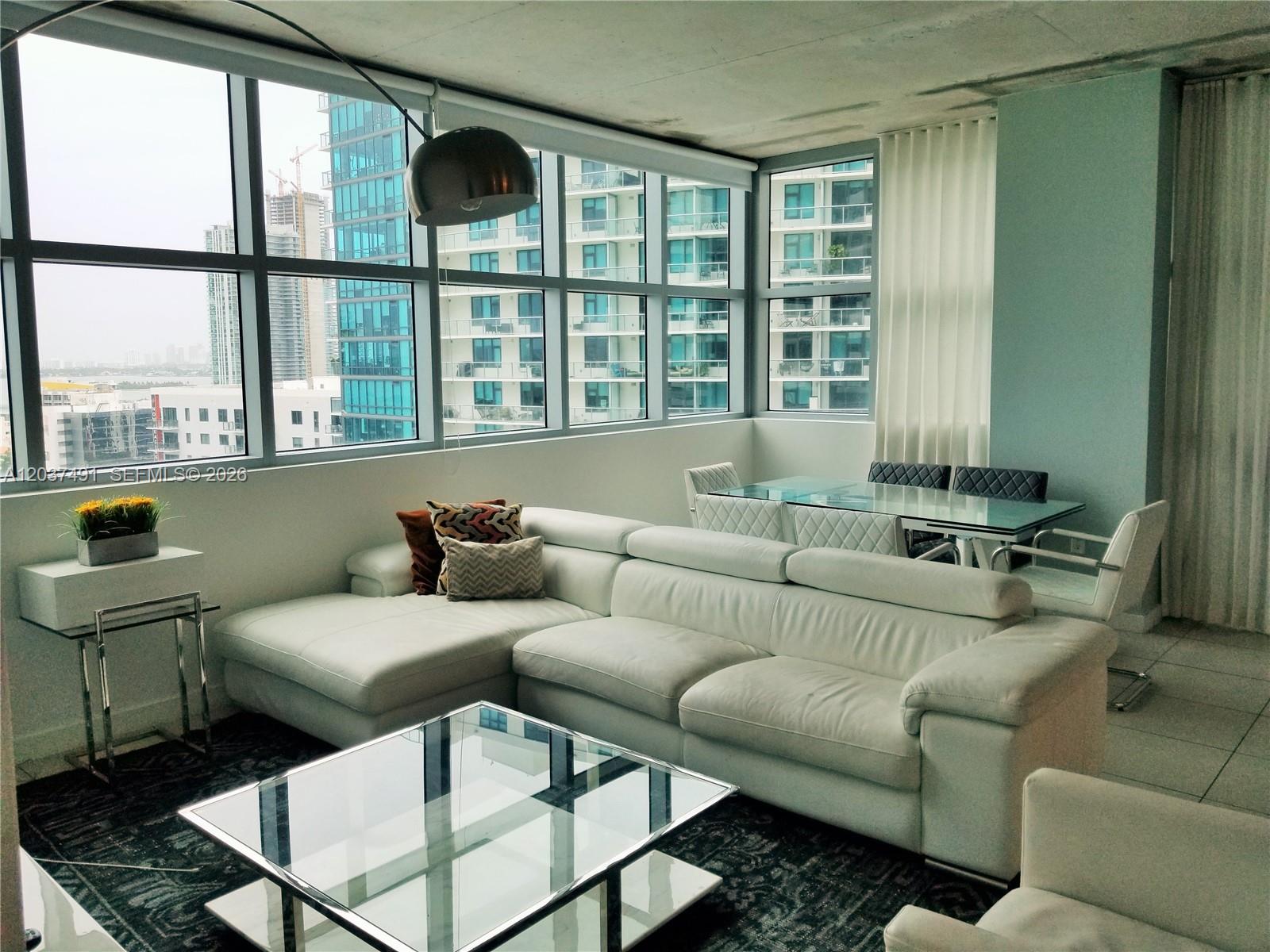 A modern living and dining area features a white sectional sofa, glass tables, and floor-to-ceiling windows — 3301 NE 1st Ave # 1602, Miami FL 33137, MIAMI, FL