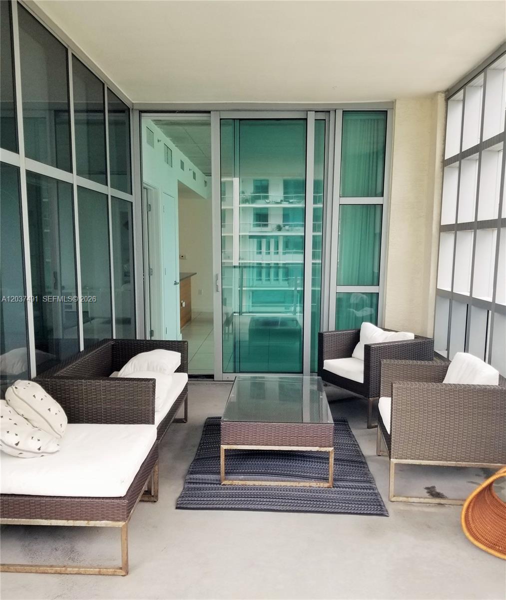 A balcony features wicker patio furniture, a glass-topped coffee table, and floor-to-ceiling glass walls — 3301 NE 1st Ave # 1602, Miami FL 33137, MIAMI, FL