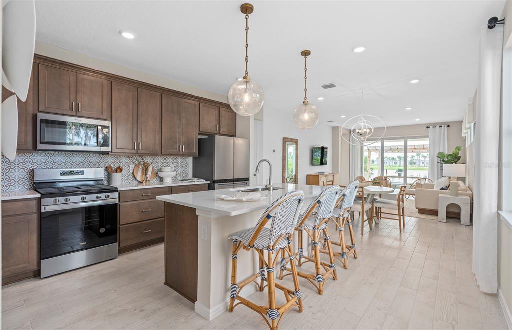 A kitchen with brown cabinets, a white island, and bar stools opens to a dining area — 6764 SUNRISE COVE DRIVE, CLERMONT, FL