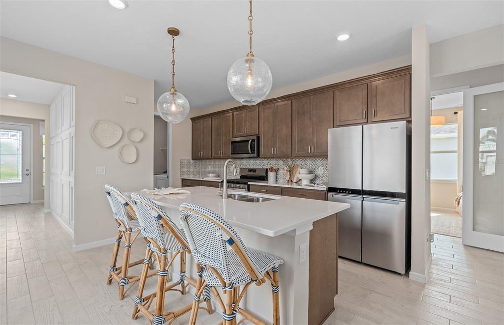 A kitchen features a white quartz island, wooden cabinets, stainless steel appliances, and three barstools — 6764 SUNRISE COVE DRIVE, CLERMONT, FL
