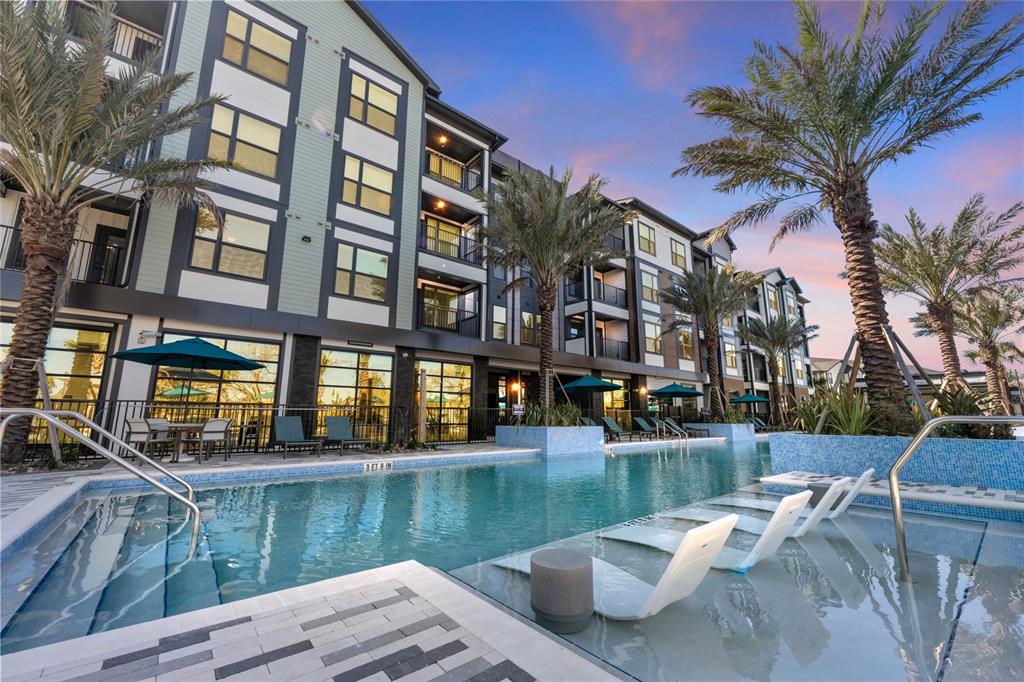 A multi-story apartment building overlooks a swimming pool with lounge chairs and palm trees — 2285 CROWN VILLAGE ROAD UNIT B3, OCOEE, FL