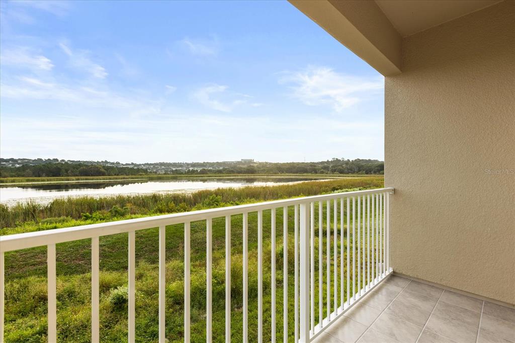 A covered balcony with a white railing overlooks a grassy field and a lake — 925 LAKEFRONT VILLAGE DRIVE, CLERMONT, FL