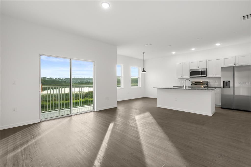 An open-concept kitchen and living area with white cabinets, stainless appliances, and a balcony view — 925 LAKEFRONT VILLAGE DRIVE, CLERMONT, FL