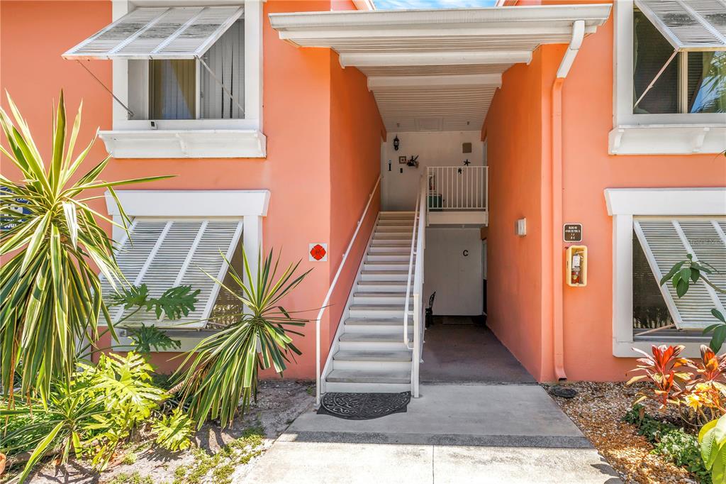 Exterior view of a peach-colored building with an outdoor staircase leading to a second-floor entrance — 4160 35TH TERRACE S UNIT I, ST PETERSBURG, FL
