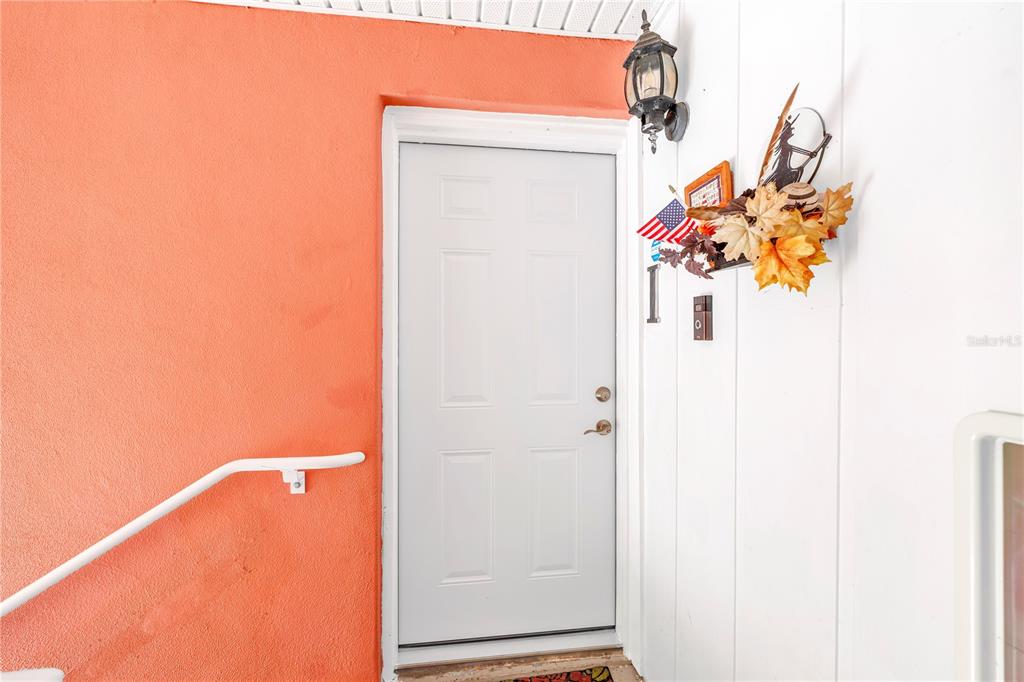 A white door with a decorative autumn wreath sits between a peach wall and white siding — 4160 35TH TERRACE S UNIT I, ST PETERSBURG, FL