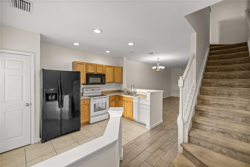 A kitchen with light wood cabinets, black appliances, and tile flooring next to a staircase — 4428 SW 49TH AVENUE, OCALA, FL