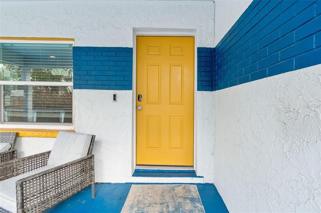 A bright yellow front door is centered on a porch with blue-painted brick accents — 1102 E RIVER COVE STREET, TAMPA, FL