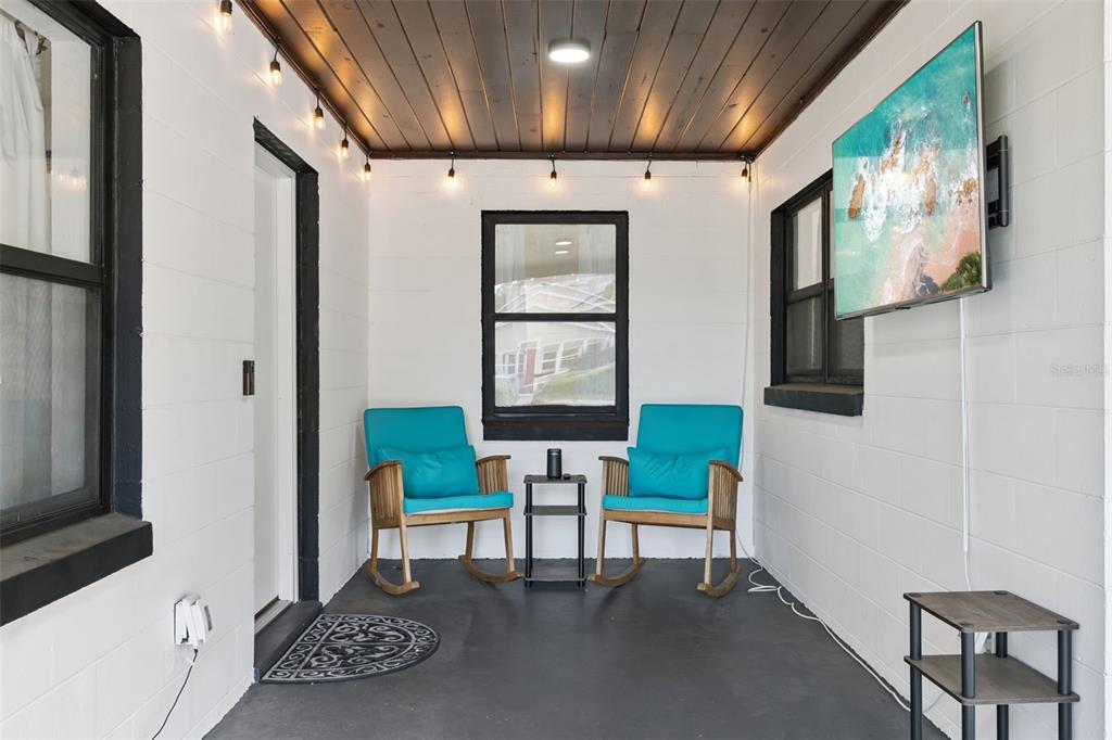 A covered porch features a dark wood ceiling, white block walls, two rocking chairs, and a television — 1915 WEBER STREET, ORLANDO, FL
