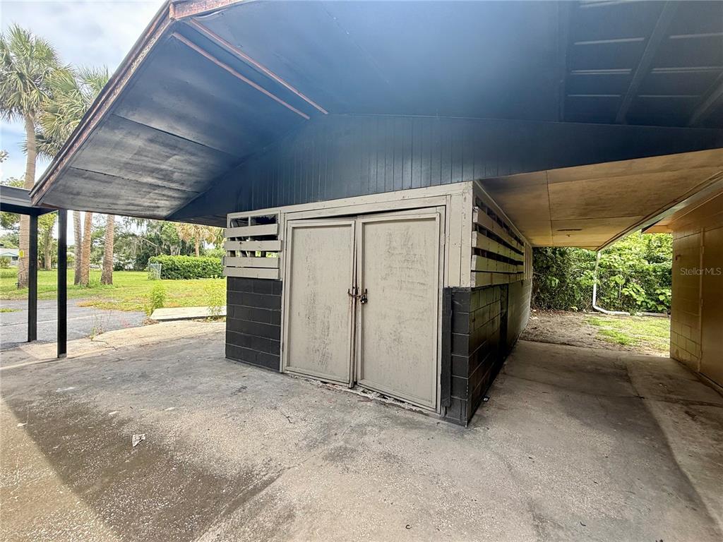 A storage shed with double doors sits under a covered carport on a concrete slab — E BATES AVENUE, EUSTIS, FL