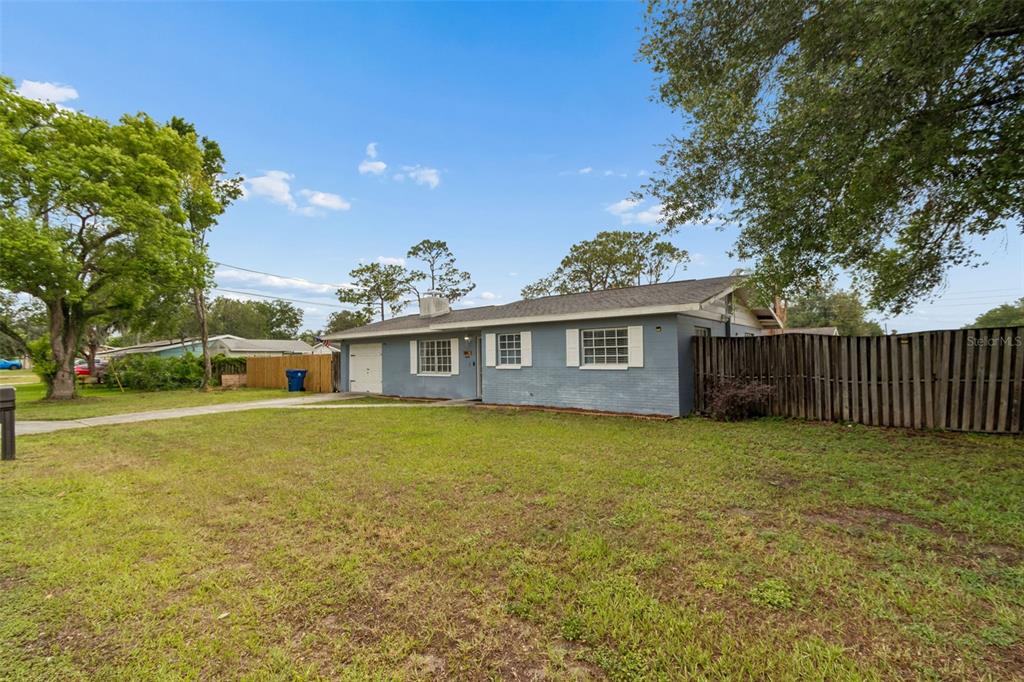 A single-story blue brick house with a white garage door and a wooden fence — 39051 12TH AVENUE, ZEPHYRHILLS, FL