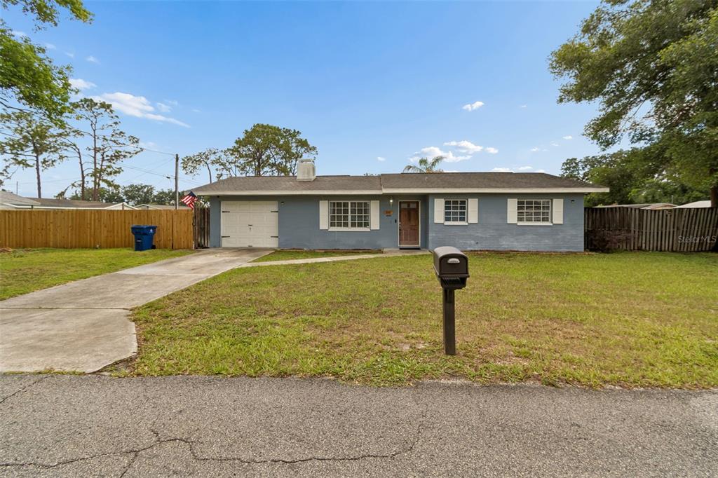 A single-story gray house with a white garage door, shutters, and a front lawn — 39051 12TH AVENUE, ZEPHYRHILLS, FL