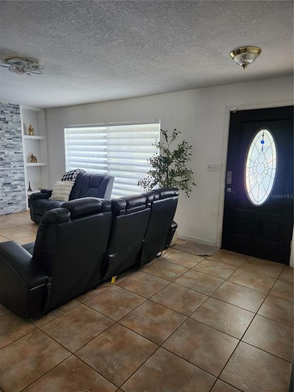 A living room features tile flooring, a black front door, and a stone fireplace wall — 1682 STARFISH STREET, KISSIMMEE, FL