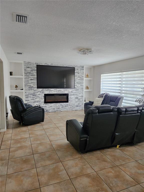 A living room features a stone-accented wall with a mounted television and electric fireplace — 1682 STARFISH STREET, KISSIMMEE, FL