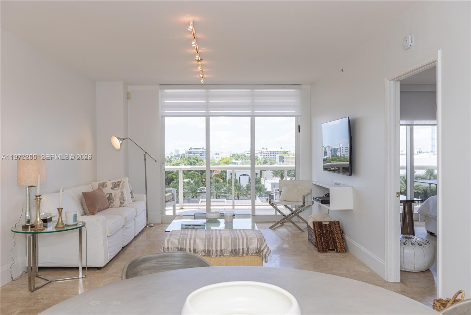 A bright living room features a white sofa, glass coffee table, and floor-to-ceiling balcony windows — 9595 Collins Ave # F, Surfside FL 33154, SURFSIDE, FL