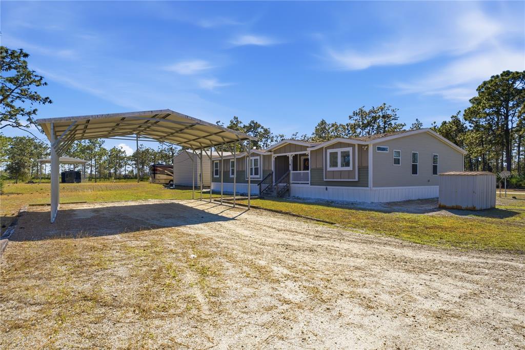 A manufactured home with a metal carport and a small storage shed on a dirt lot — 6844 CHAD JASON ROAD, ST CLOUD, FL