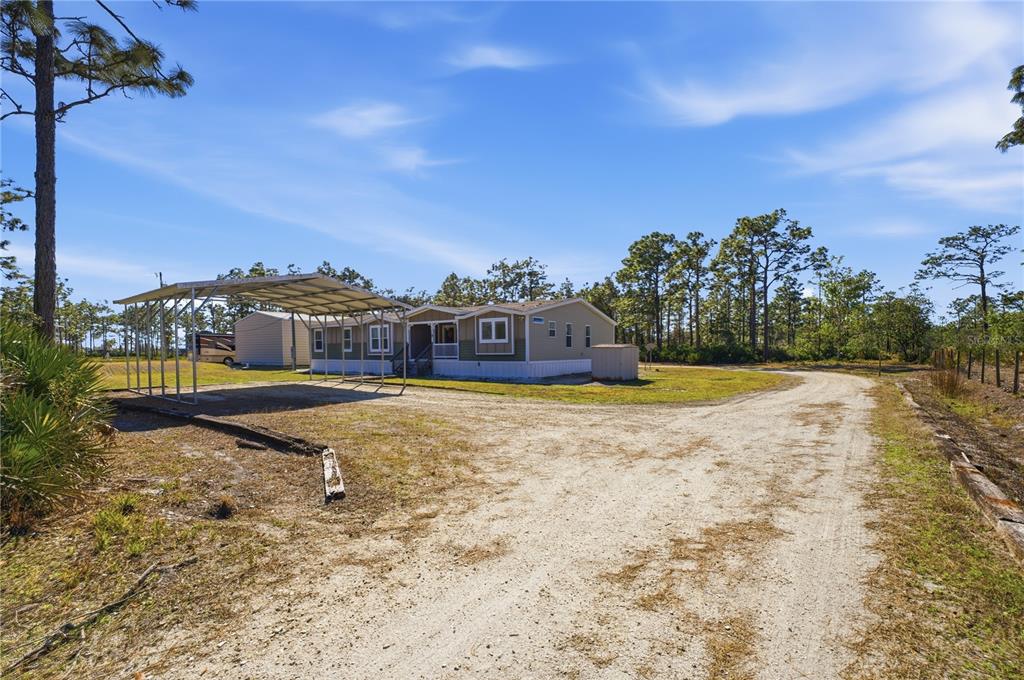 A manufactured home with a metal carport sits on a dirt lot surrounded by trees — 6844 CHAD JASON ROAD, ST CLOUD, FL
