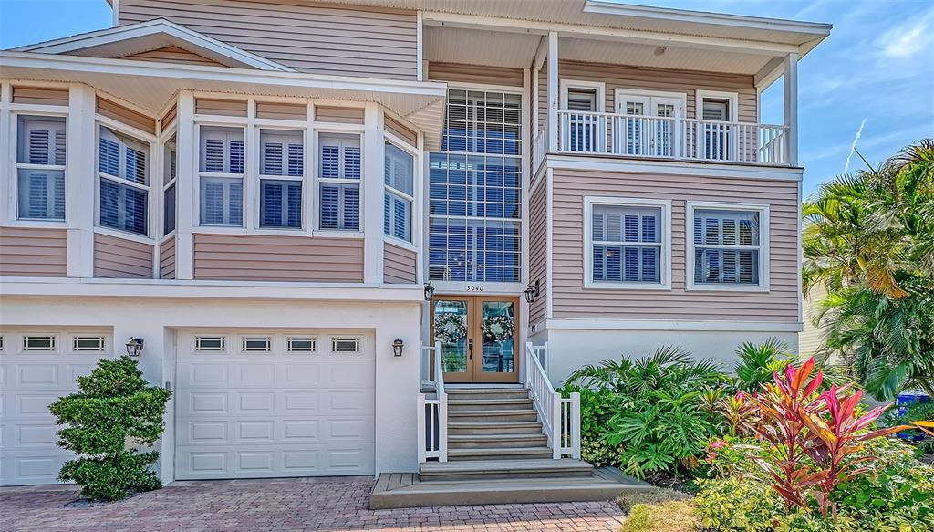 A multi-story house features light-colored siding, a two-car garage, and a front staircase entrance — 3040 GULF OF MEXICO DRIVE UNIT 3, LONGBOAT KEY, FL