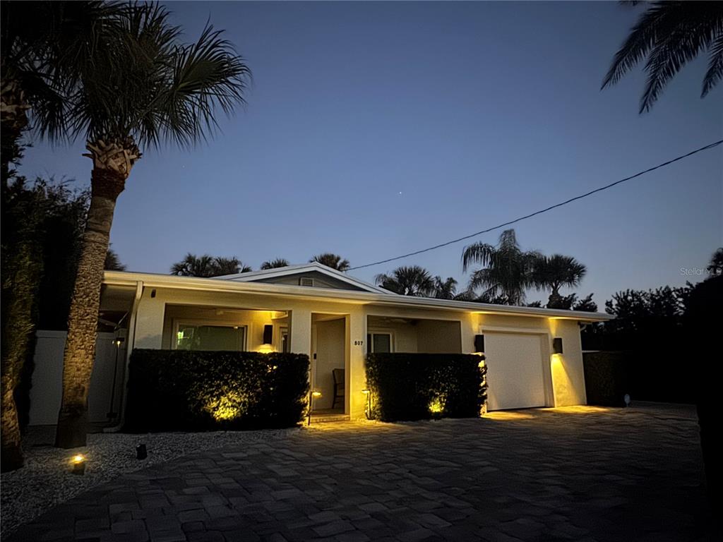 A single-story house with a paved driveway, palm trees, and exterior landscape lighting at dusk — 507 N PENINSULA AVENUE, NEW SMYRNA BEACH, FL