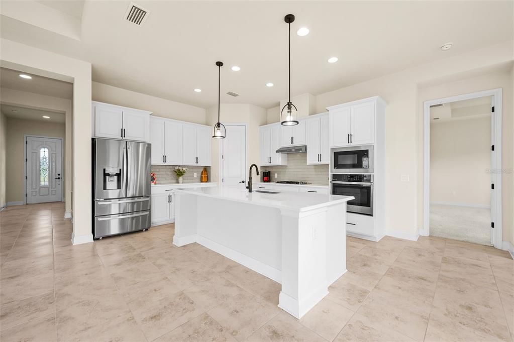A modern kitchen features white cabinetry, a central island, stainless steel appliances, and tile flooring — 3612 SW 120TH TERRACE, GAINESVILLE, FL