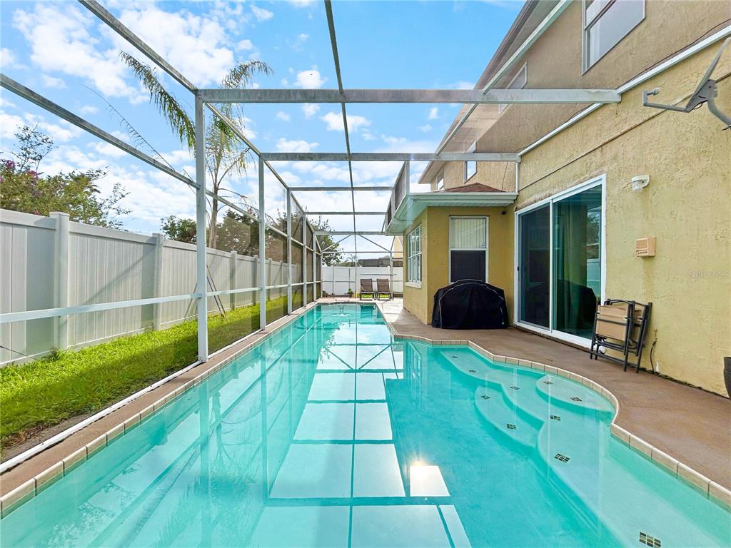 A screened-in swimming pool with built-in steps sits beside a two-story house and fence — 1606 WOOD VIOLET DRIVE, ORLANDO, FL