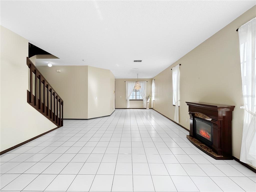 A long, empty room features white tile flooring, a wooden staircase, and a fireplace — 1606 WOOD VIOLET DRIVE, ORLANDO, FL