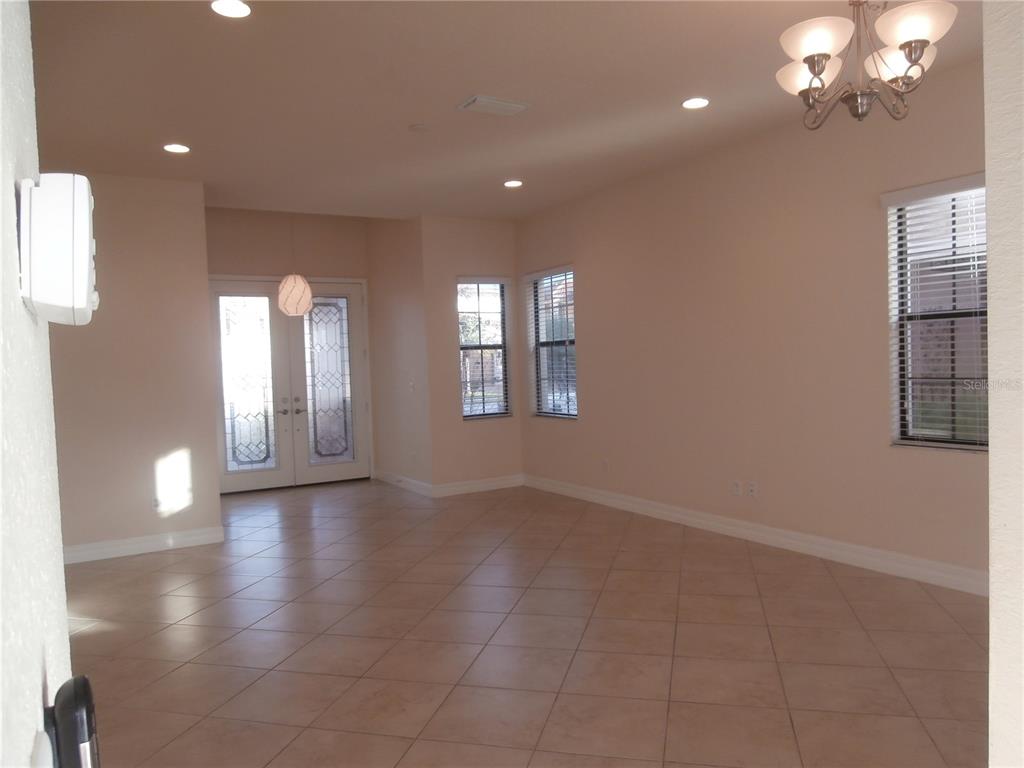 An empty room with beige tile flooring, light walls, a chandelier, and double front doors — 13172 WOODFORD STREET, ORLANDO, FL