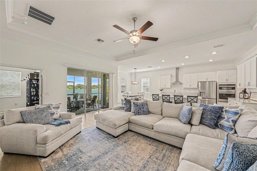 A spacious open-concept living room features a large sectional sofa, neutral decor, and sliding glass doors — 12840 BERGSTROM BAY DRIVE, RIVERVIEW, FL