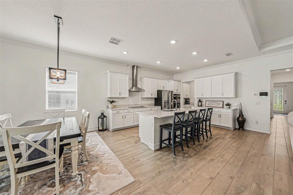 A bright, open-concept kitchen features white cabinetry, a central island, and wood-look tile flooring — 12840 BERGSTROM BAY DRIVE, RIVERVIEW, FL