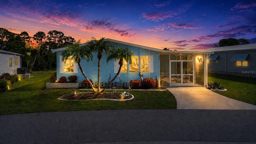 A light blue manufactured home with a screened porch and palm trees at sunset — 608 PORTSIDE DRIVE, NORTH PORT, FL