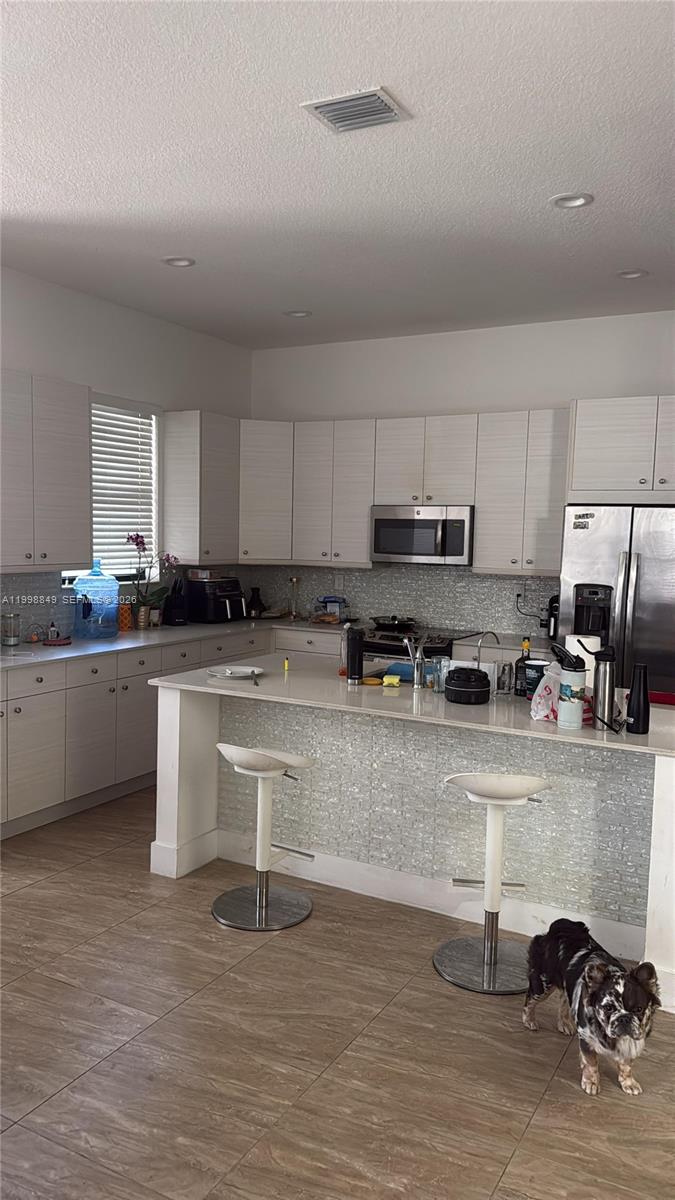 A kitchen with white cabinets, a tiled island, stainless steel appliances, and a small dog — 3564 W 97th St, Hialeah FL 33018, HIALEAH, FL