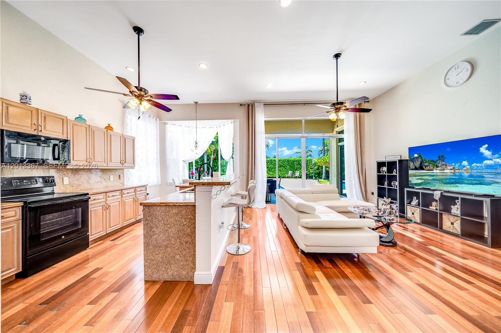 An open-concept kitchen and living area features wood flooring, light cabinetry, and a sliding glass door — 1241 S 13th Ave, Hollywood FL 33019, HOLLYWOOD, FL