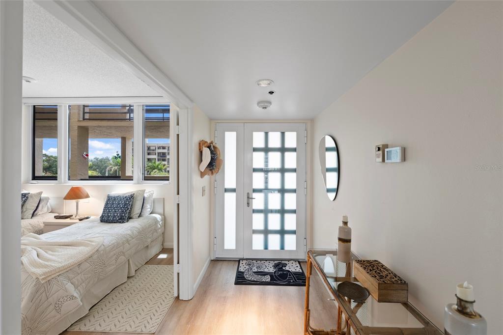 An entryway with a glass-paneled door leads into a bedroom featuring a bed and windows — 1095 GULF OF MEXICO DRIVE UNIT 303, LONGBOAT KEY, FL