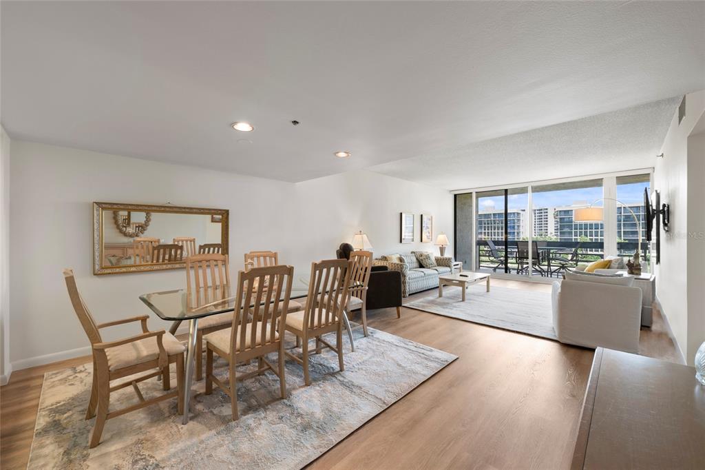 An open-concept living and dining area features wood-look flooring, a glass dining table, and balcony — 1095 GULF OF MEXICO DRIVE UNIT 303, LONGBOAT KEY, FL