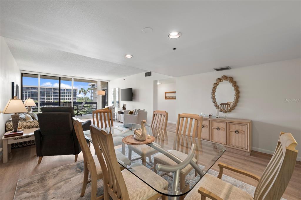 An open-concept living and dining area features wood-look flooring, a glass-top table, and balcony access — 1095 GULF OF MEXICO DRIVE UNIT 303, LONGBOAT KEY, FL