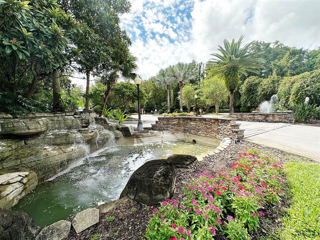A stone waterfall flows into a pond beside a landscaped garden and paved driveway — 5124 CONROY ROAD UNIT 12, ORLANDO, FL