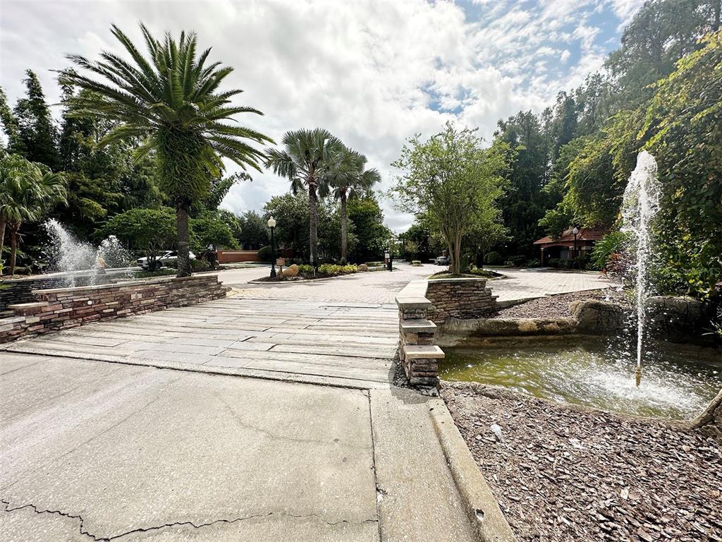 A paved entrance features stone-walled fountains, palm trees, and a landscaped driveway — 5124 CONROY ROAD UNIT 12, ORLANDO, FL